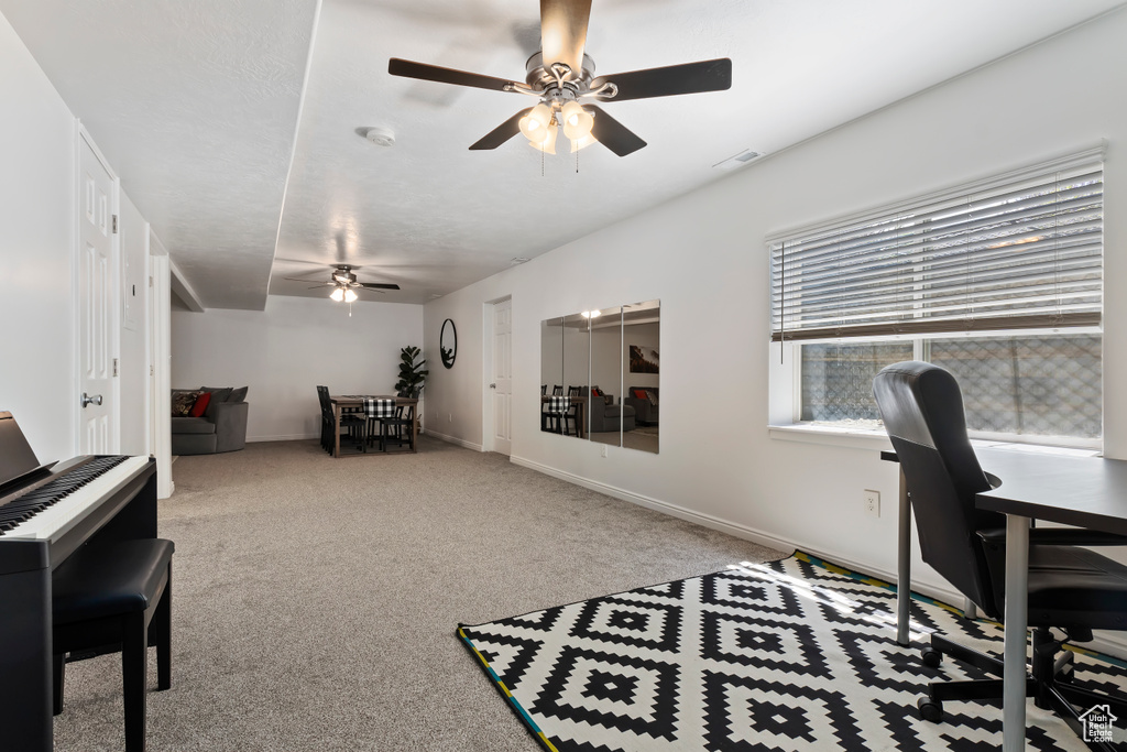 Carpeted office space featuring ceiling fan and baseboards