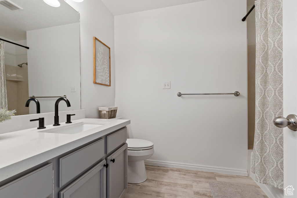 Bathroom featuring wood finished floors, vanity, toilet, shower / bath combo, and baseboards