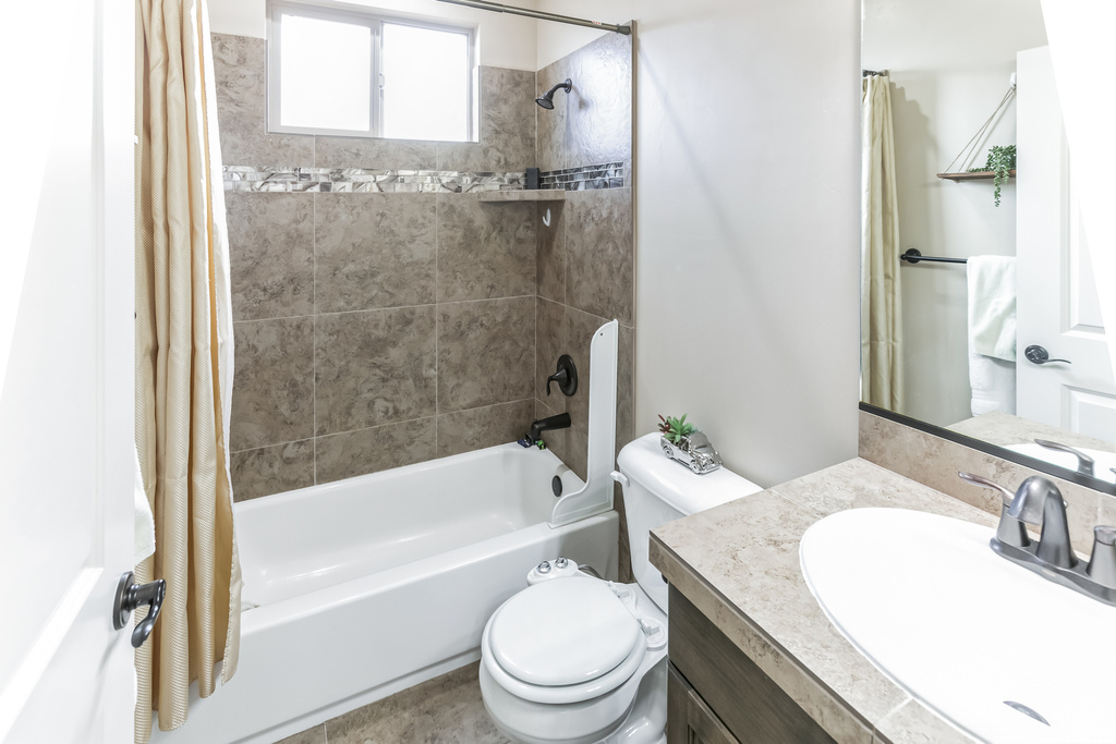 Bathroom with shower / bathtub combination with curtain, vanity, and toilet