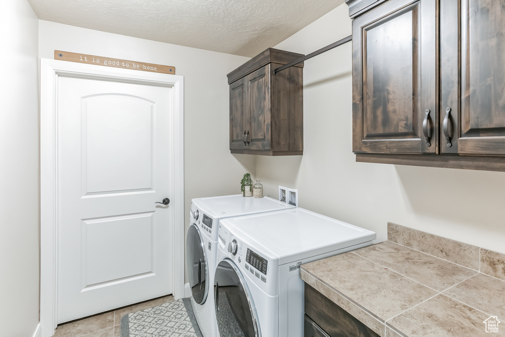 Washroom with cabinet space, washing machine and dryer, light tile patterned flooring, and a textured ceiling