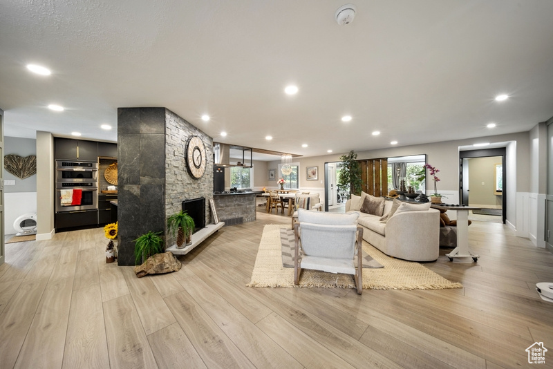 Living room with light wood-style floors, a wainscoted wall, recessed lighting, and a stone fireplace