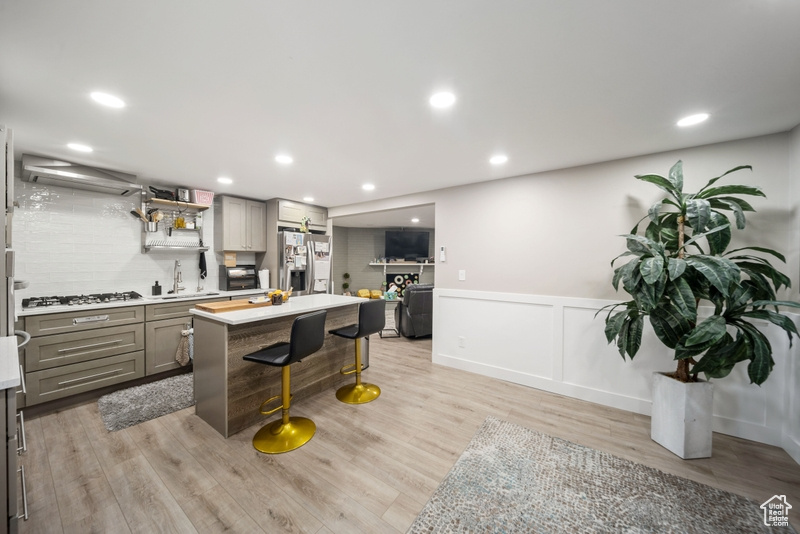 Kitchen featuring gray cabinetry, stainless steel refrigerator with ice dispenser, a breakfast bar, light countertops, and light wood-type flooring