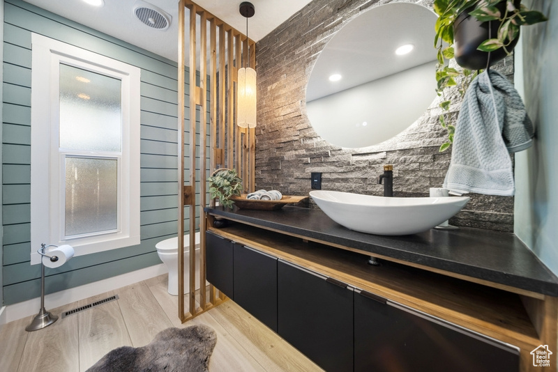 Bathroom featuring toilet, vanity, wood finished floors, and wooden walls