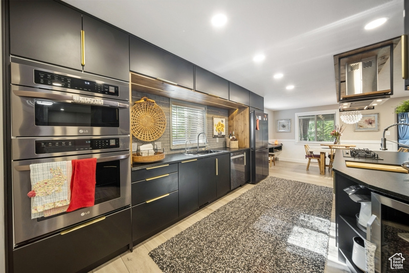 Kitchen with appliances with stainless steel finishes, recessed lighting, wine cooler, light wood-type flooring, and dark countertops