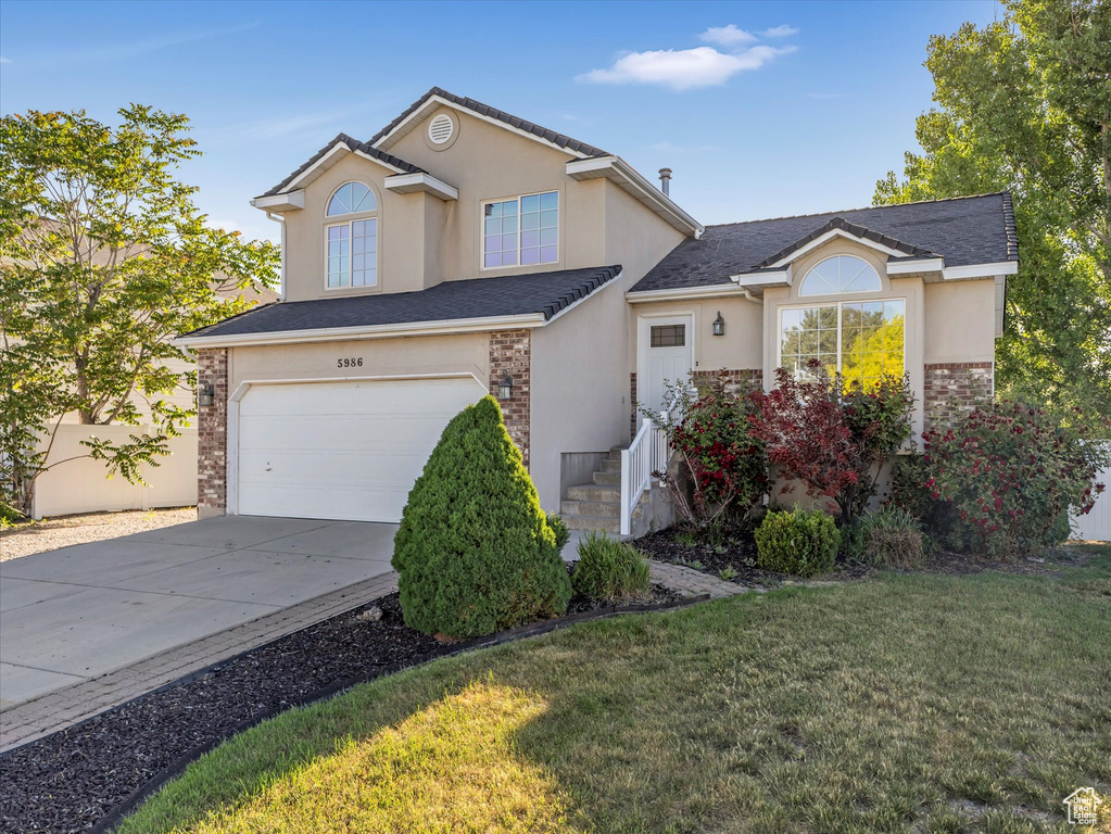 Traditional home with stucco siding, an attached garage, concrete driveway, and a front lawn