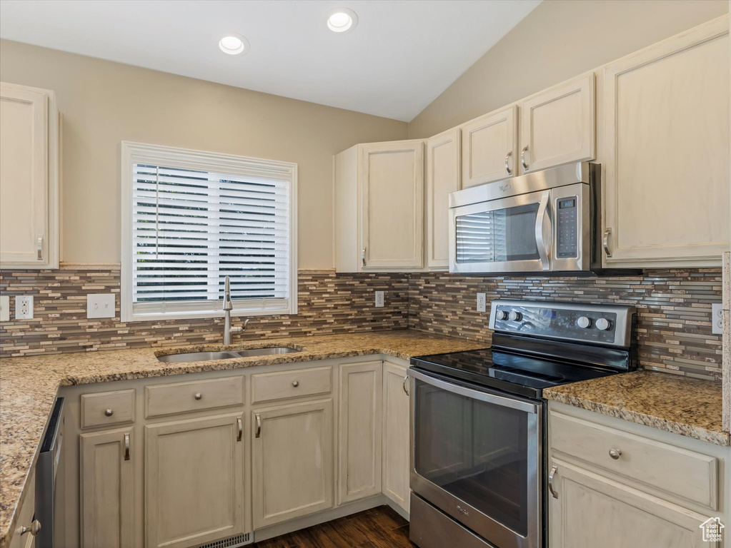Kitchen featuring appliances with stainless steel finishes, a sink, lofted ceiling, decorative backsplash, and light stone counters