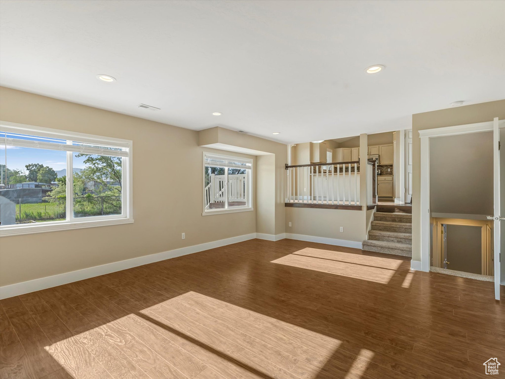 Unfurnished living room featuring plenty of natural light, wood finished floors, baseboards, stairway, and recessed lighting