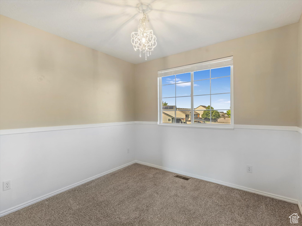 Carpeted spare room with a chandelier and baseboards