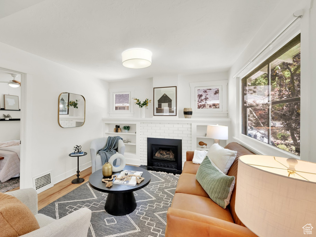 Living room with wood finished floors, a brick fireplace, baseboards, and ceiling fan
