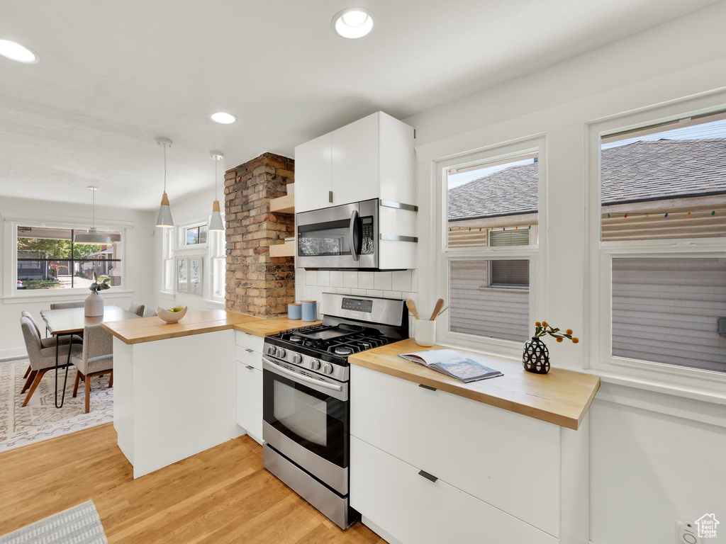 Kitchen featuring appliances with stainless steel finishes, wooden counters, light wood-type flooring, white cabinetry, and tasteful backsplash