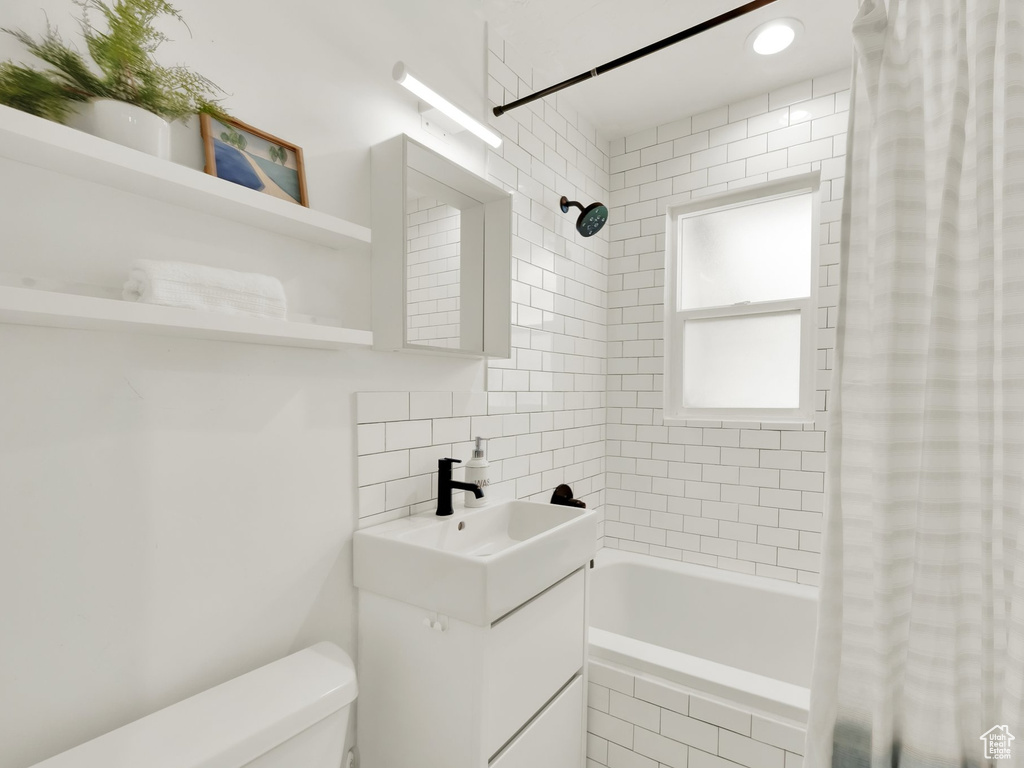 Bathroom with vanity, tiled shower / bath, toilet, and decorative backsplash