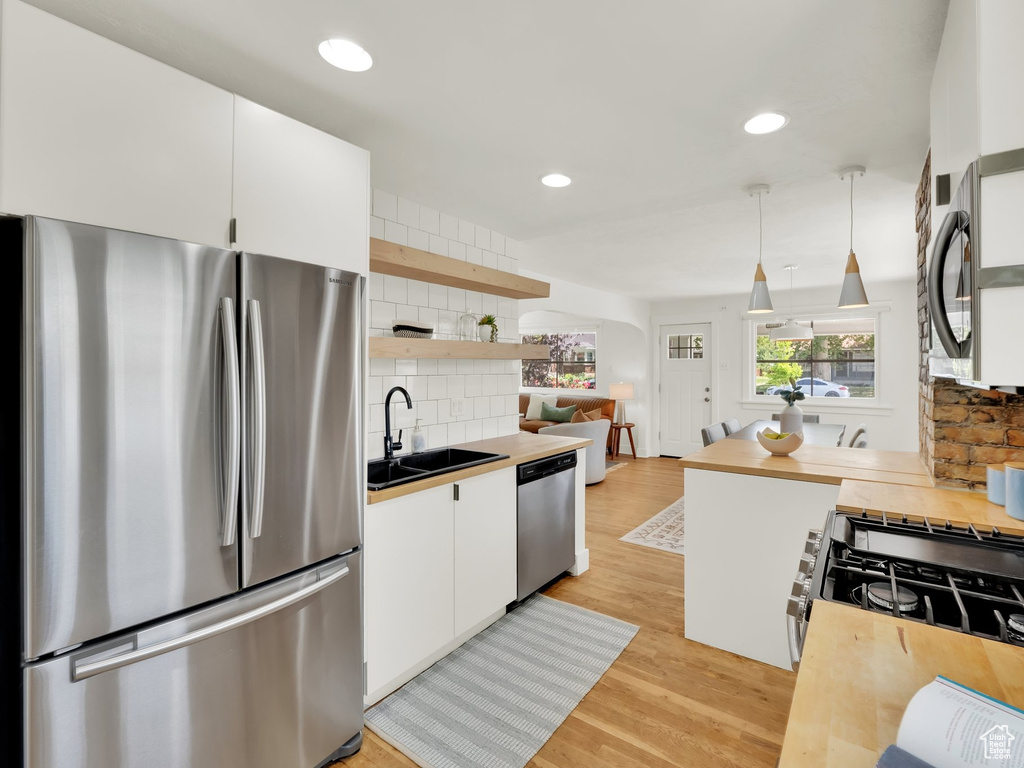 Kitchen with stainless steel appliances, a sink, backsplash, white cabinetry, and open shelves