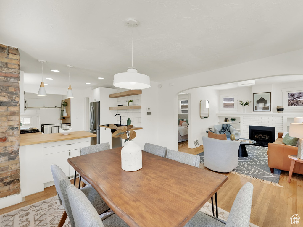 Dining room with arched walkways, a brick fireplace, light wood-style flooring, and recessed lighting