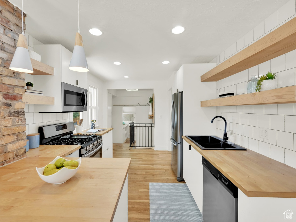 Kitchen with open shelves, butcher block counters, a sink, stainless steel appliances, and recessed lighting