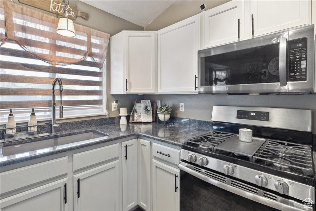 Kitchen featuring stainless steel appliances, a sink, white cabinets, lofted ceiling, and dark stone countertops