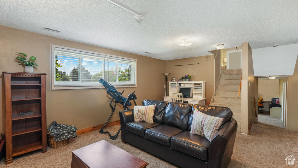 Living area featuring light carpet, stairs, and a textured ceiling