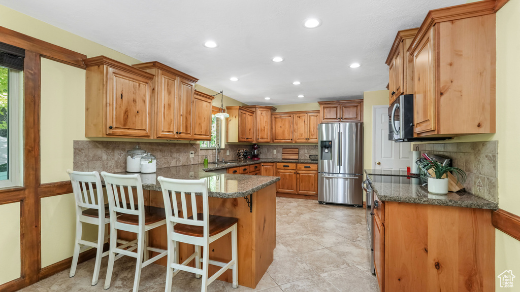 Kitchen featuring appliances with stainless steel finishes, a peninsula, tasteful backsplash, a sink, and a breakfast bar