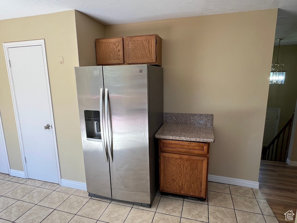Kitchen with stainless steel refrigerator with ice dispenser, brown cabinetry, light tile patterned flooring, and baseboards
