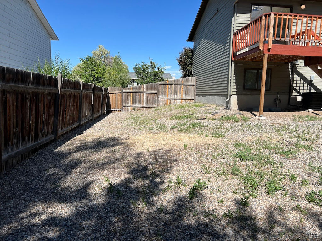 Fenced backyard with a wooden deck, central AC unit, and stairway
