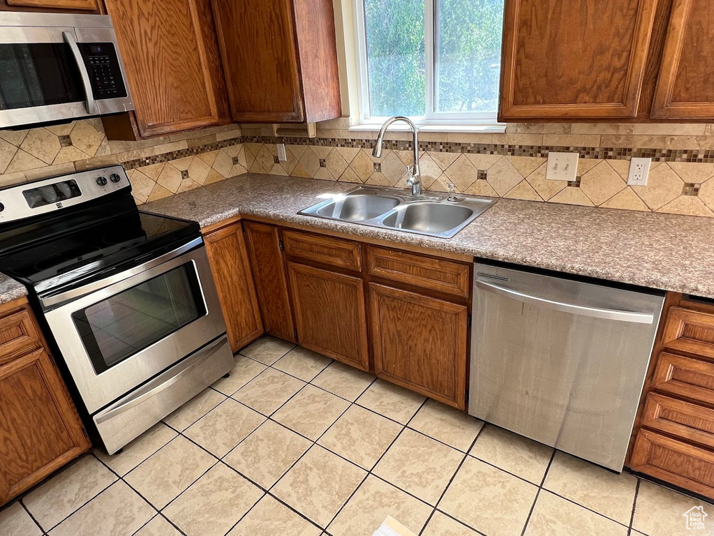 Kitchen with stainless steel appliances, a sink, light tile patterned flooring, and backsplash