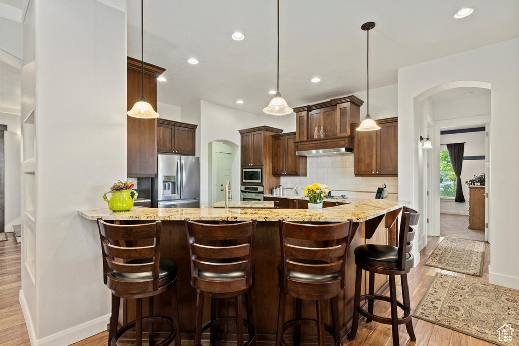 Kitchen featuring stainless steel appliances, arched walkways, light wood finished floors, baseboards, and tasteful backsplash