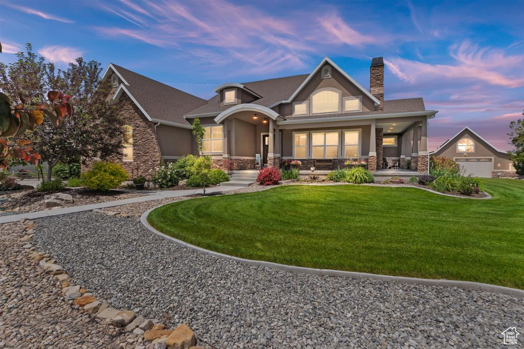 View of front of home featuring stone siding, covered porch, a chimney, and a lawn