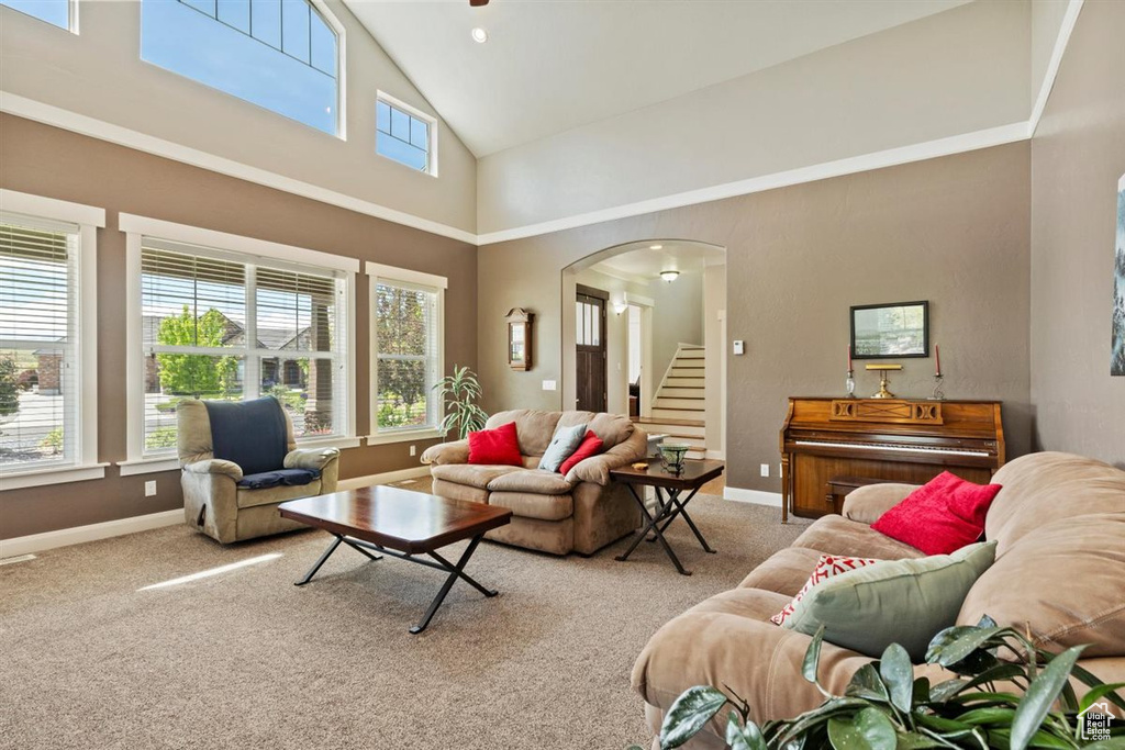 Carpeted living area with plenty of natural light, high vaulted ceiling, stairway, baseboards, and arched walkways