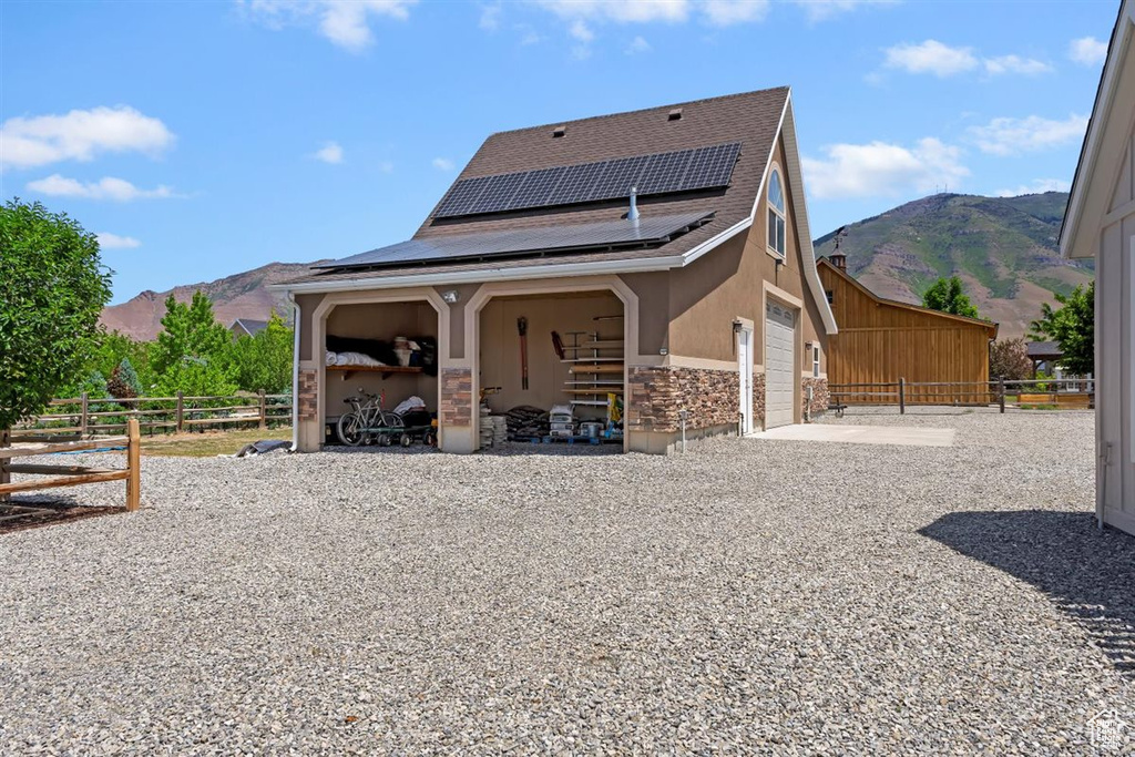 Back of house with a mountain view, solar panels, stucco siding, and stone siding