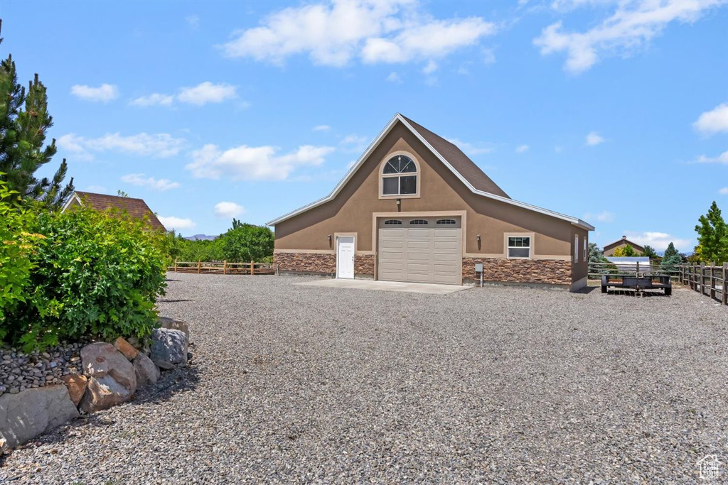 View of side of home featuring stucco siding, stone siding, a detached garage, and driveway