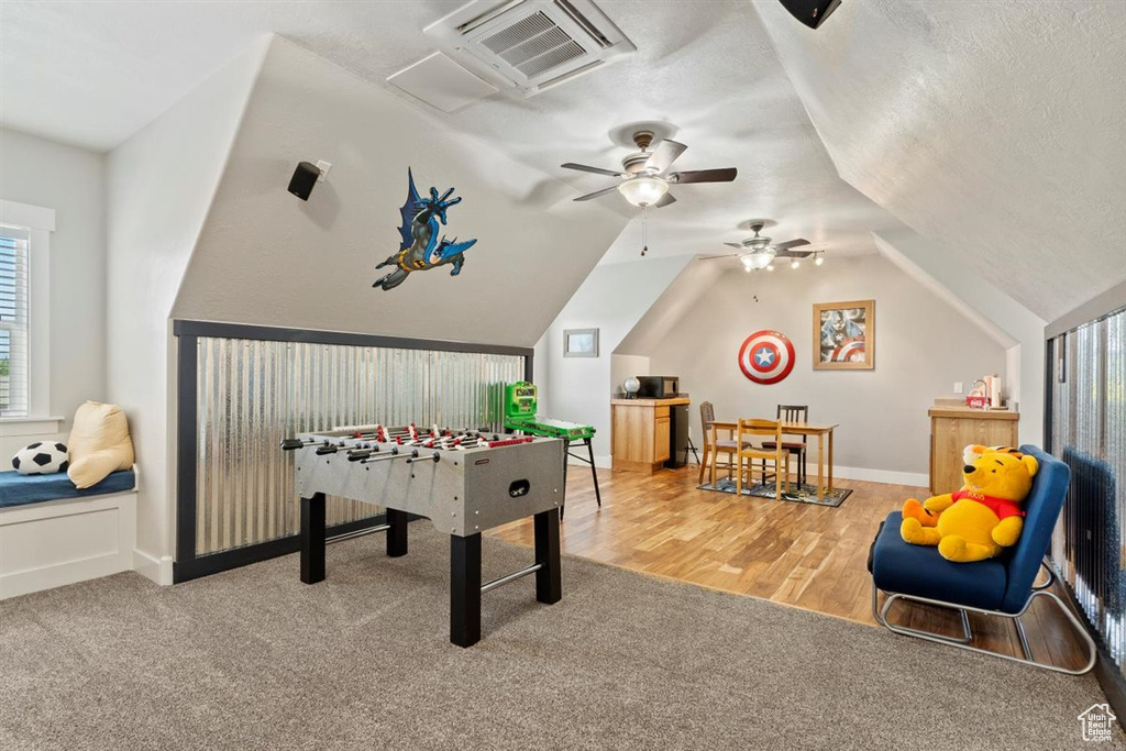 Recreation room with a ceiling fan, vaulted ceiling, carpet, baseboards, and a textured ceiling