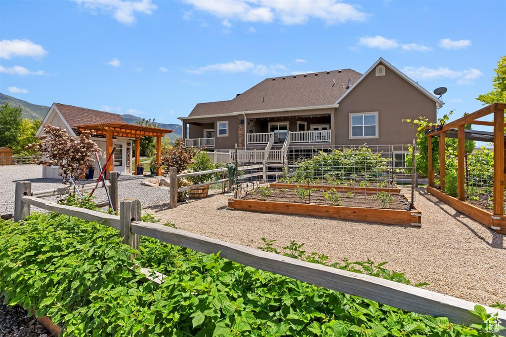 Back of property featuring a vegetable garden, a pergola, and stucco siding