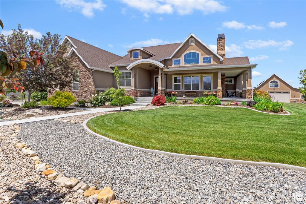 Craftsman house featuring stone siding, stucco siding, a chimney, a front lawn, and covered porch