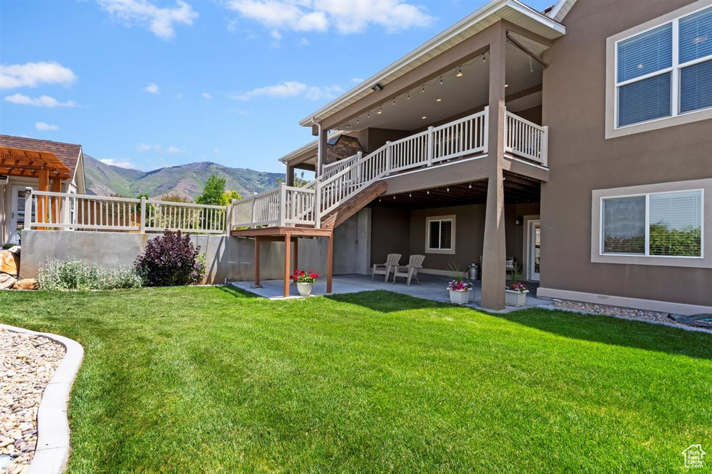 Rear view of house with a patio area, stucco siding, a lawn, and a deck with mountain view