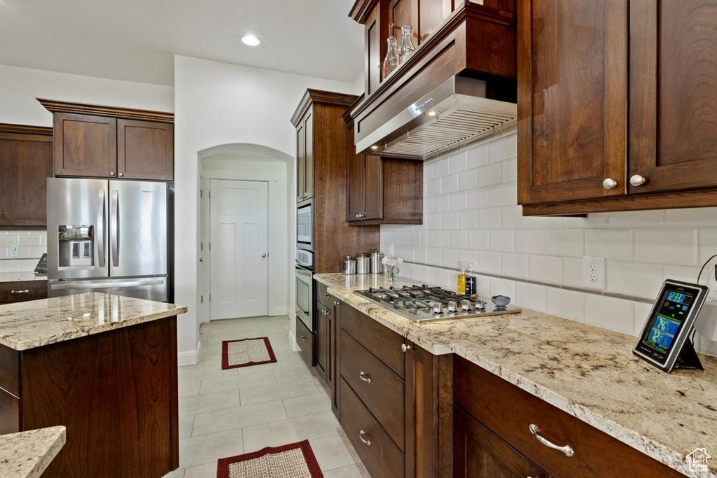 Kitchen featuring appliances with stainless steel finishes, extractor fan, arched walkways, backsplash, and light tile patterned floors
