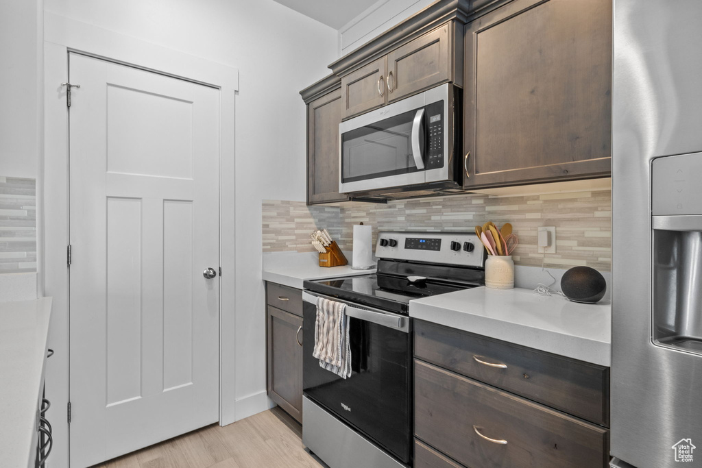 Kitchen with stainless steel appliances, light countertops, tasteful backsplash, light wood-style floors, and dark brown cabinetry