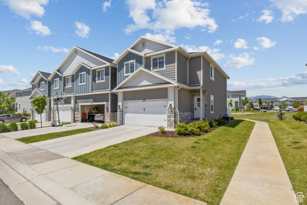 View of property with board and batten siding, driveway, a front yard, stone siding, and a residential view