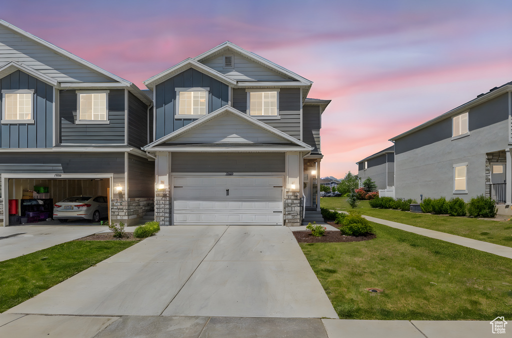 View of front facade featuring board and batten siding, driveway, a garage, a yard, and stone siding