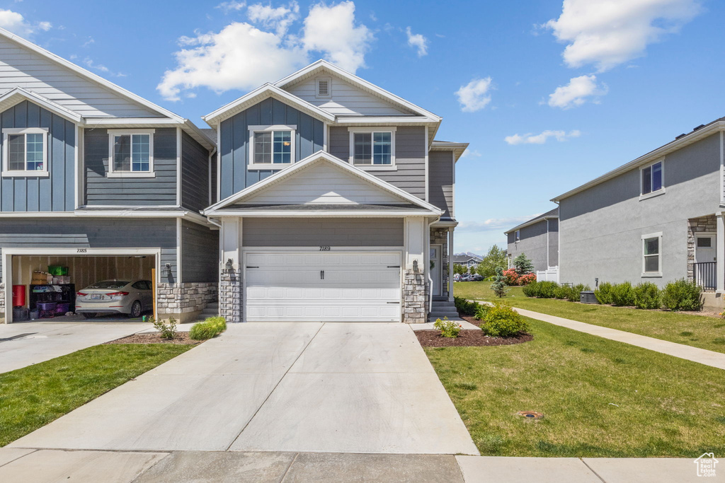 View of front of house featuring board and batten siding, a garage, a front lawn, concrete driveway, and stone siding