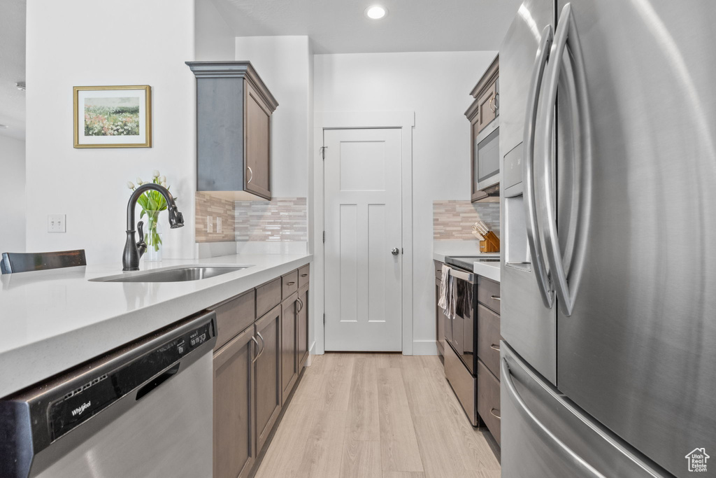 Kitchen with appliances with stainless steel finishes, a sink, light wood-style floors, decorative backsplash, and light countertops