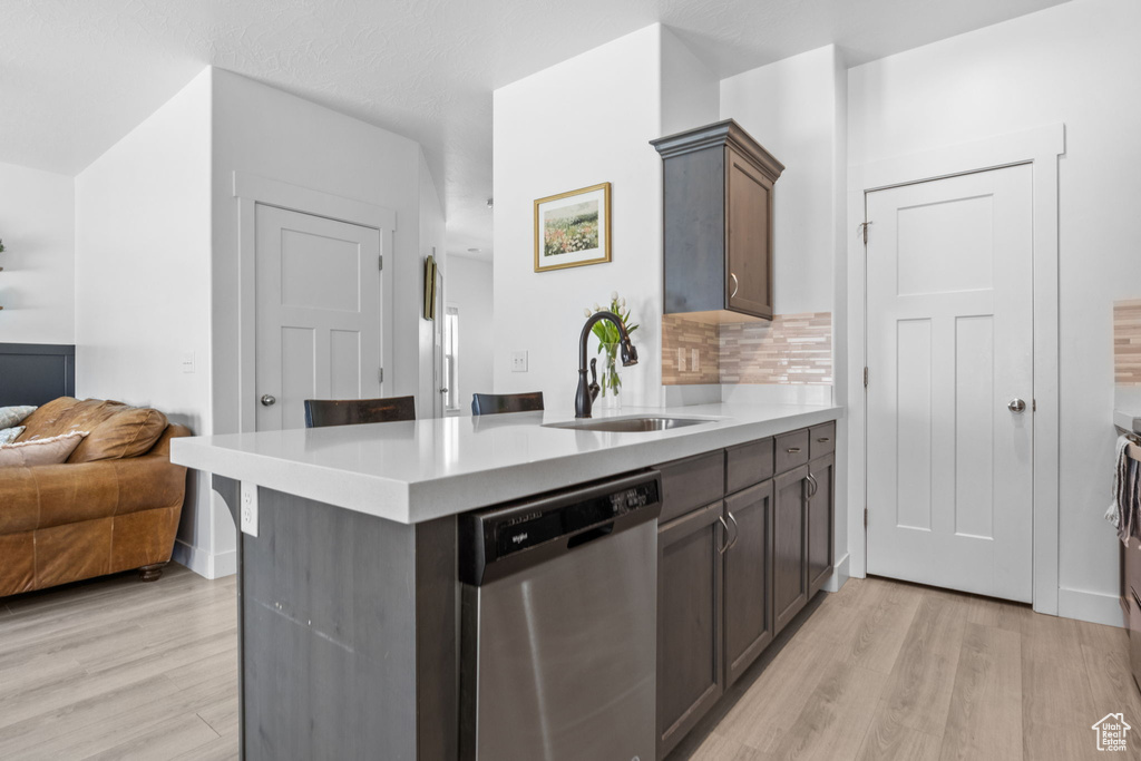 Kitchen featuring dishwasher, a sink, light wood-style floors, and light countertops