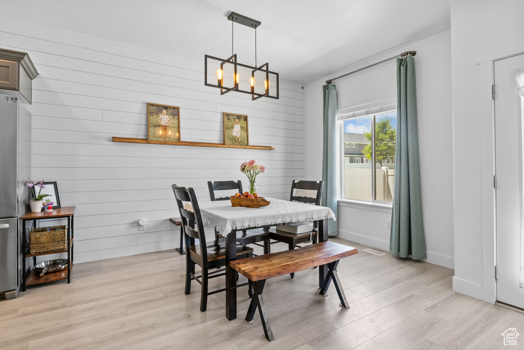 Dining room with light wood-type flooring, a chandelier, wooden walls, and baseboards