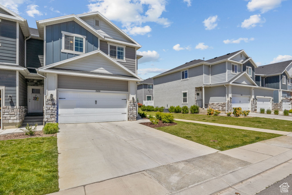 View of front of house featuring board and batten siding, stone siding, a garage, a front yard, and driveway