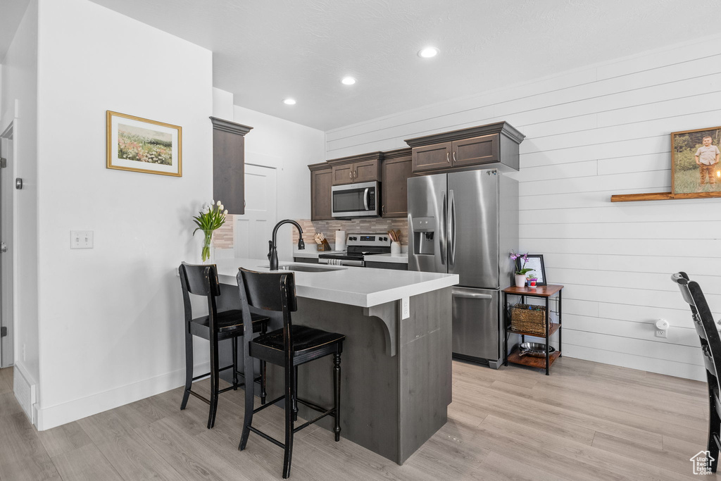 Kitchen with appliances with stainless steel finishes, a sink, a breakfast bar area, dark brown cabinetry, and a peninsula
