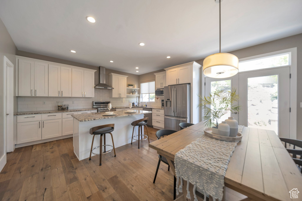 Kitchen featuring appliances with stainless steel finishes, wall chimney range hood, white cabinets, a center island, and tasteful backsplash