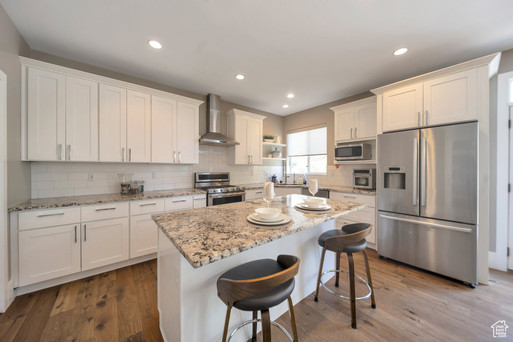 Kitchen featuring stainless steel appliances, wall chimney exhaust hood, white cabinetry, a sink, and recessed lighting