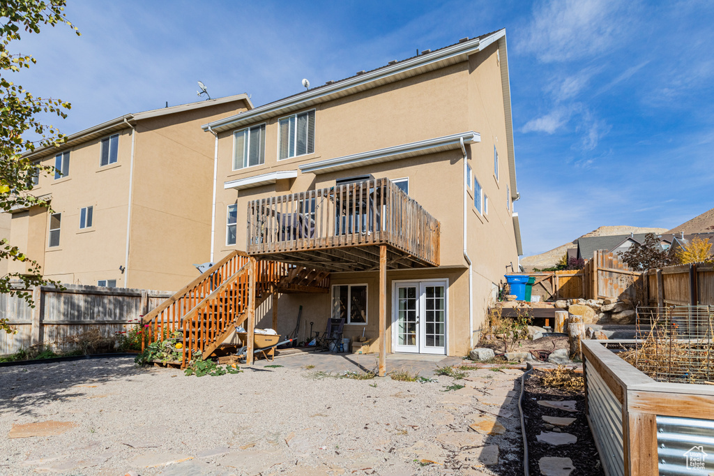 Rear view of property with a deck, stucco siding, stairs, and french doors