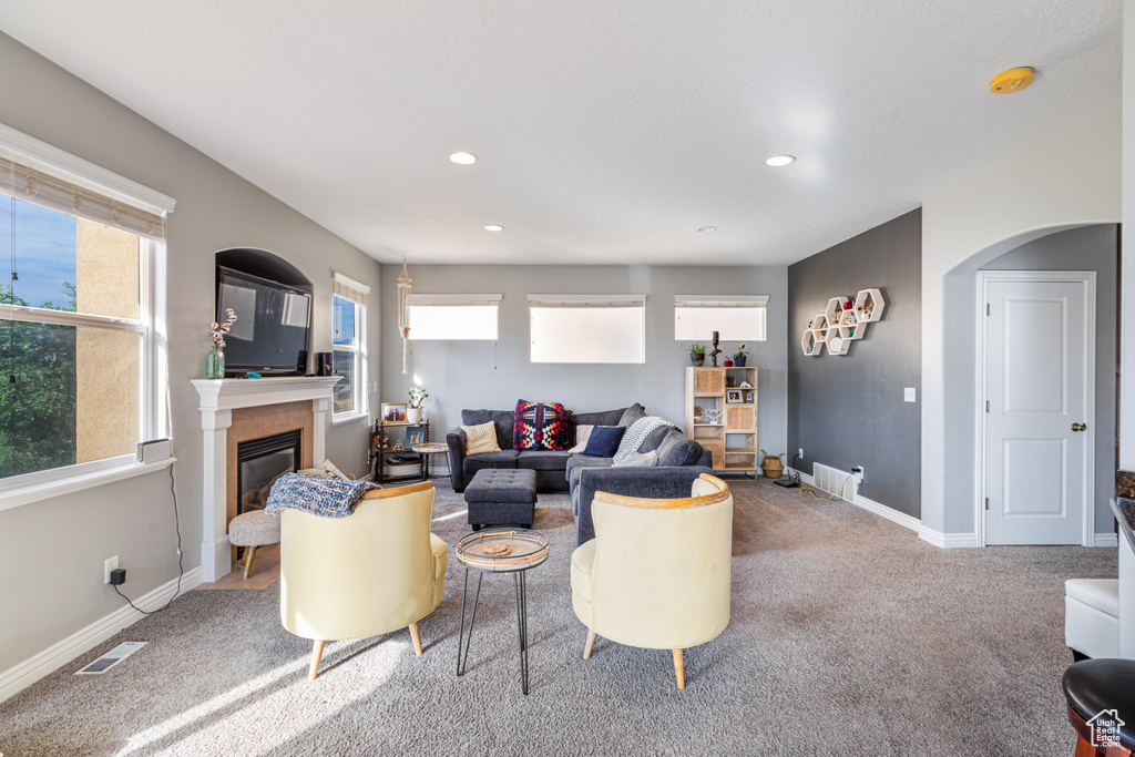 Living area with carpet floors, arched walkways, a glass covered fireplace, baseboards, and recessed lighting