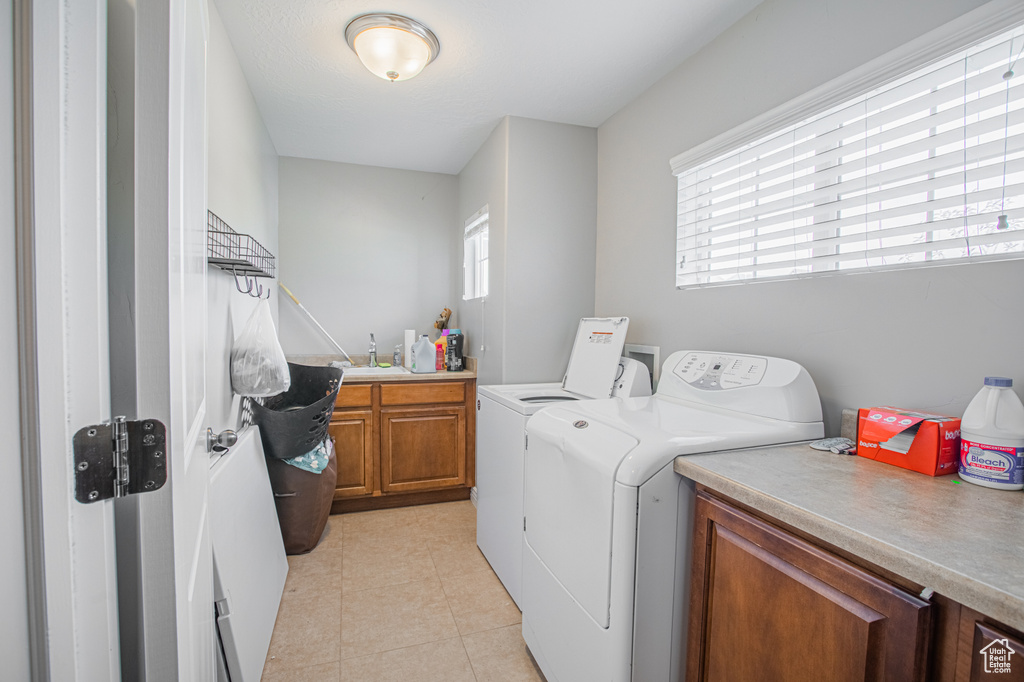 Washroom featuring washer and clothes dryer, cabinet space, and light tile patterned flooring
