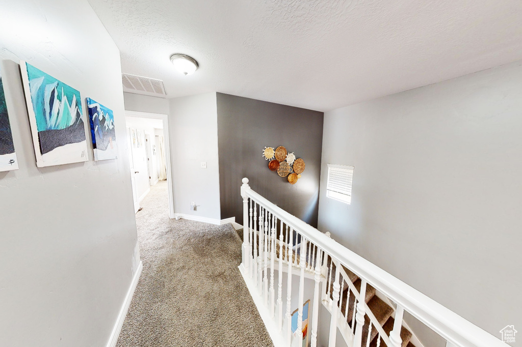 Hallway with an upstairs landing, carpet, baseboards, and a textured ceiling