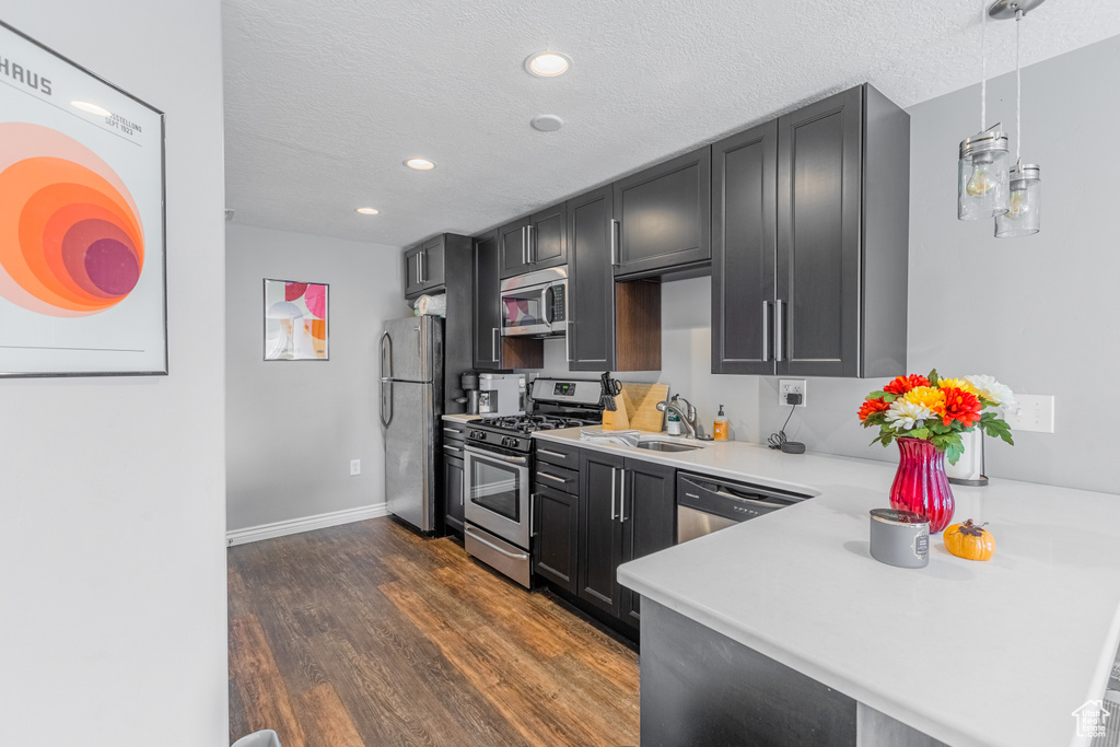 Kitchen with appliances with stainless steel finishes, dark wood finished floors, light countertops, a sink, and a peninsula